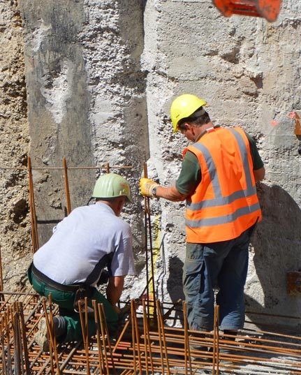 Trabajadores en obra realizando tareas de construcción en pared de concreto.