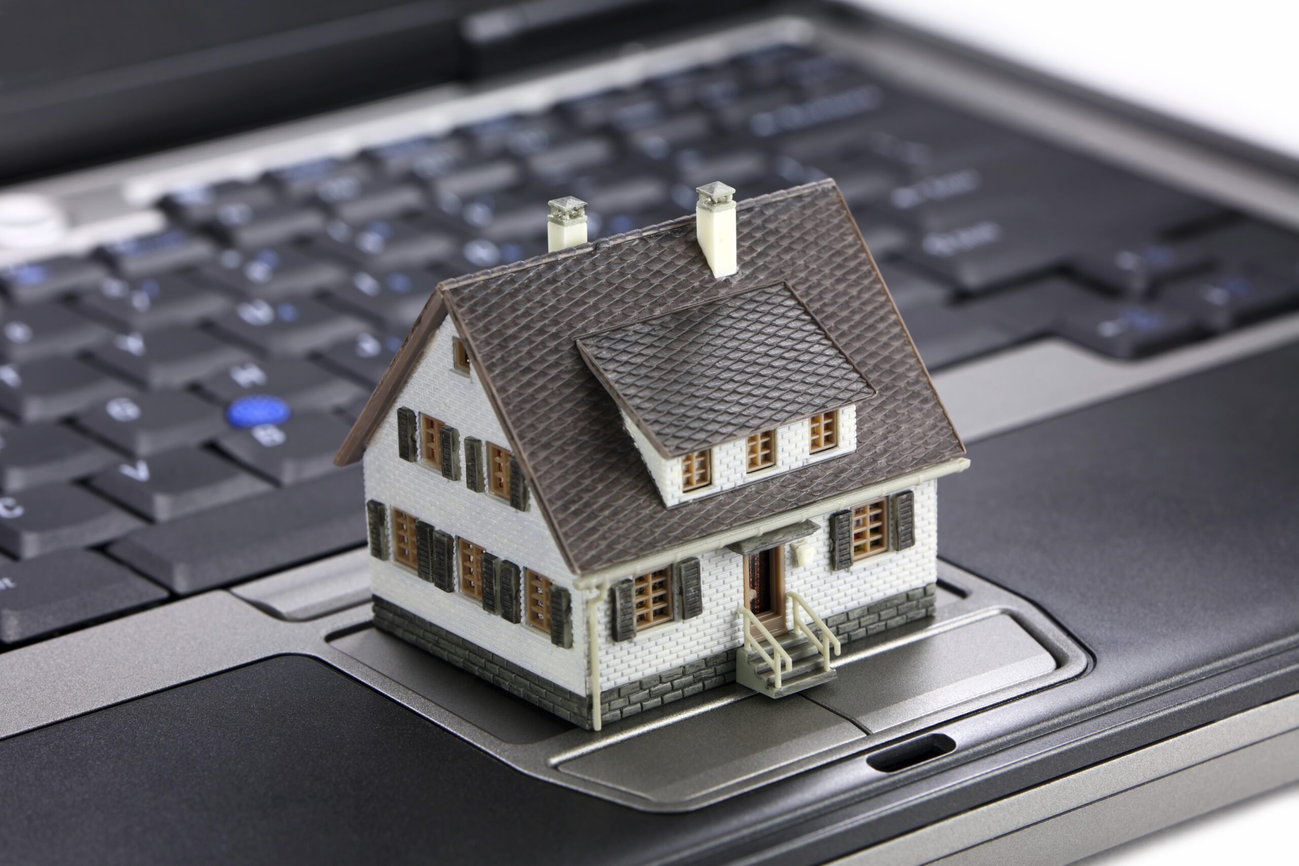 Casa en miniatura sobre teclado de laptop, representando proyectos de remodelación y desarrollo inmo.